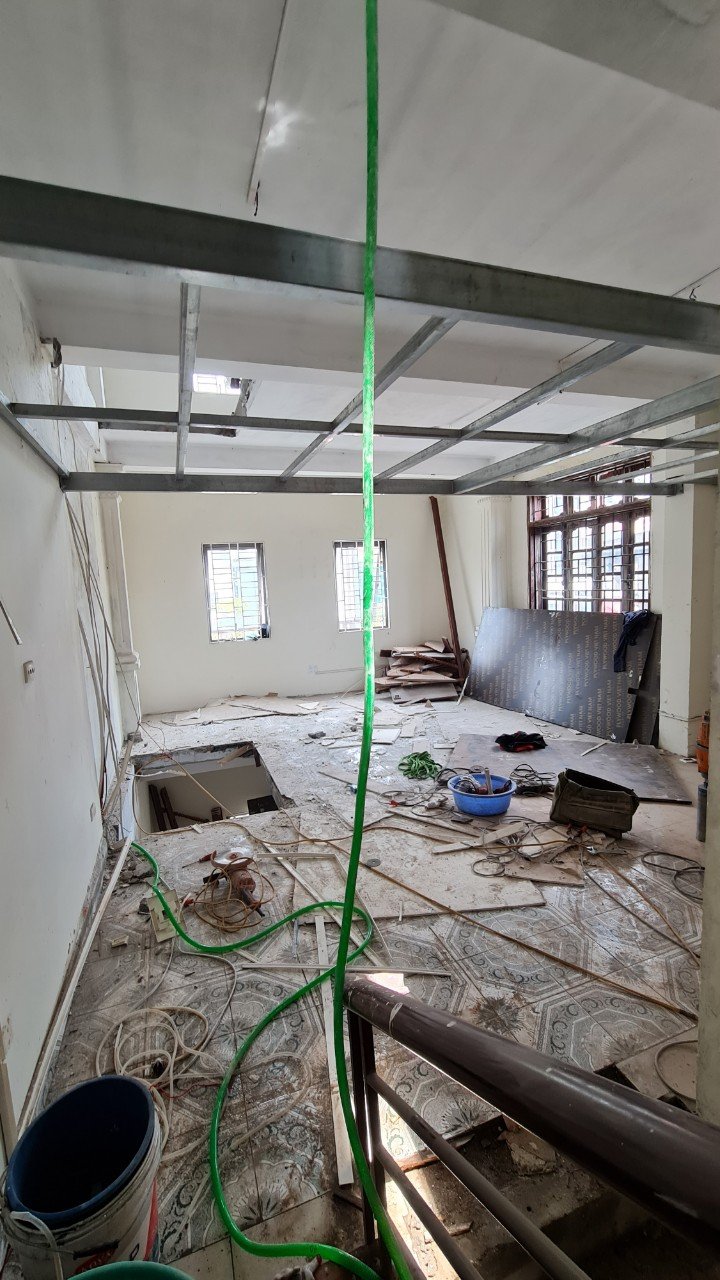 Hình ảnh thi công cải tạo nội thất với hệ thống trần đang được lắp đặt và vật liệu xây dựng bố trí trong phòng.