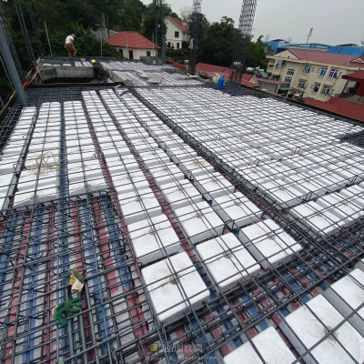 Một bức ảnh chụp từ trên cao của một sàn rỗng đang thi công, hiển thị một lưới cốt thép dày đặc bao phủ một lớp các khối xốp rỗng hình vuông màu trắng của hệ thống sàn xốp ACIF, với hai công nhân ở phía xa.